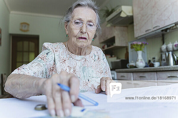 Senior woman counting money and doing paperwork at home