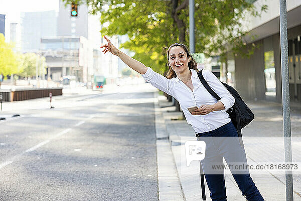 Happy businesswoman hailing for ride standing at footpath