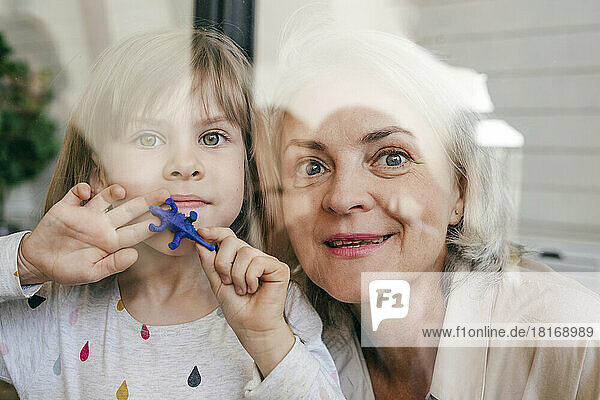 Thoughtful grandmother and granddaughter with toy looking out of window