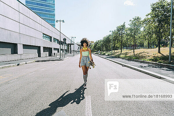 Woman with skateboard walking on road