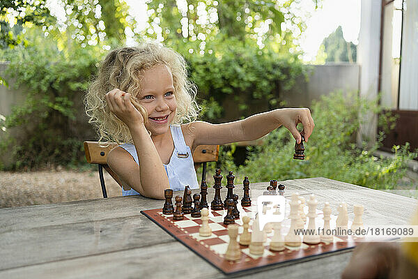 Smiling girl playing chess in garden