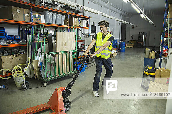 Blue-collar worker pulling hand truck in warehouse