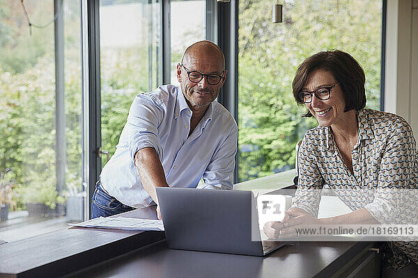 Happy senior man with woman using laptop on kitchen counter at home