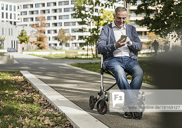 Smiling senior man using smart phone sitting on mobility walker