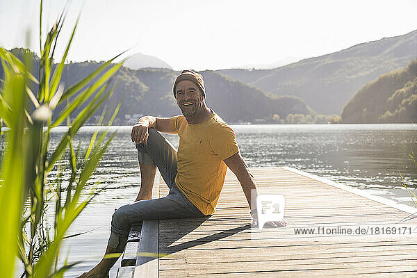 Happy mature man sitting on jetty over lake at vacation