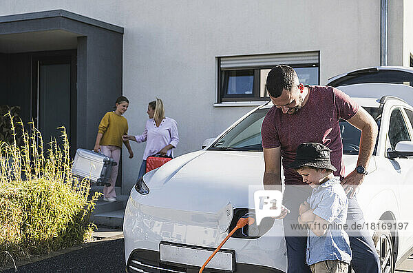 Father and son checking smartphone by charging electric car