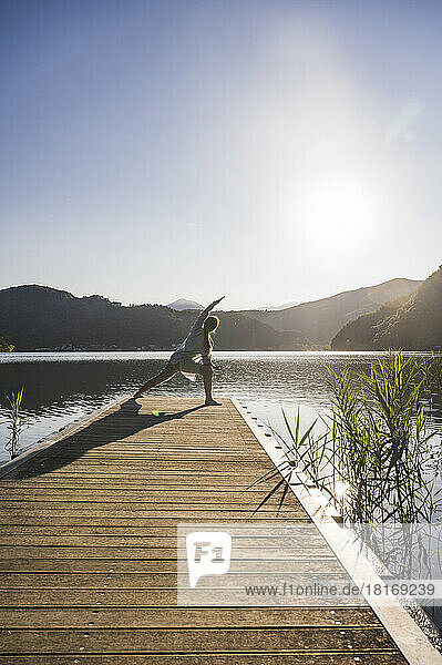 Woman stretching on jetty over lake by mountains