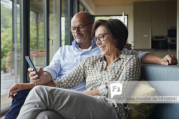 Happy woman with man using smart phone sitting on sofa at home