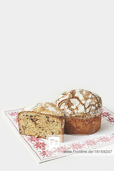 Whole and sliced panettone cake on embroidered napkin against white background