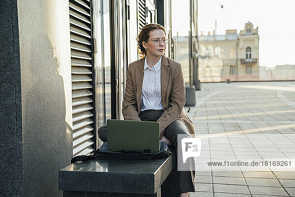 Thoughtful young freelancer with laptop sitting on bench