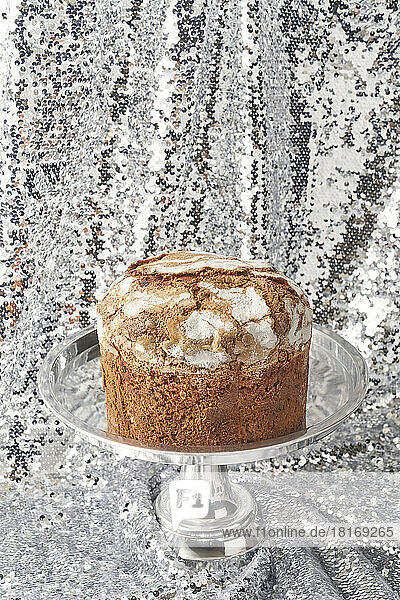 Freshly baked panettone cake on cakestand against shiny silver sequins