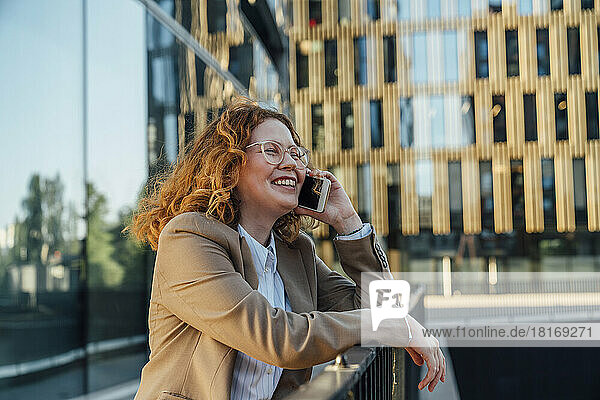Happy businesswoman talking on mobile phone in front of office building