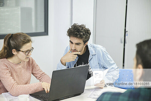 Businesswoman using laptop and discussing with colleague in office