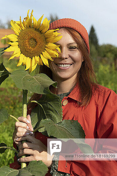 Smiling woman with brown hair holding sunflower in garden