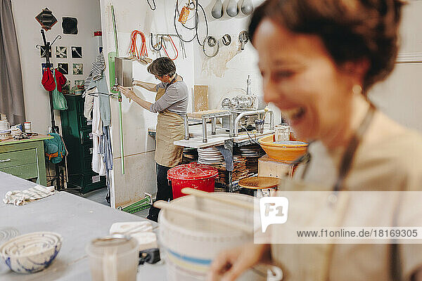 Happy entrepreneur with colleague working in background at ceramics workshop