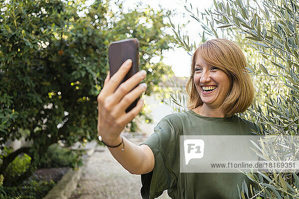 Happy mature woman taking selfie through smart phone in garden
