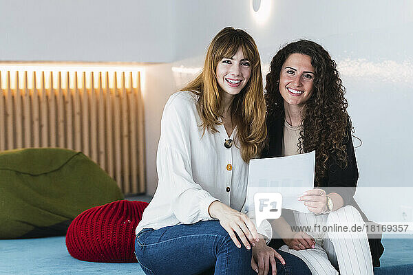 Portrait of two smiling businesswomen holding document in office lounge