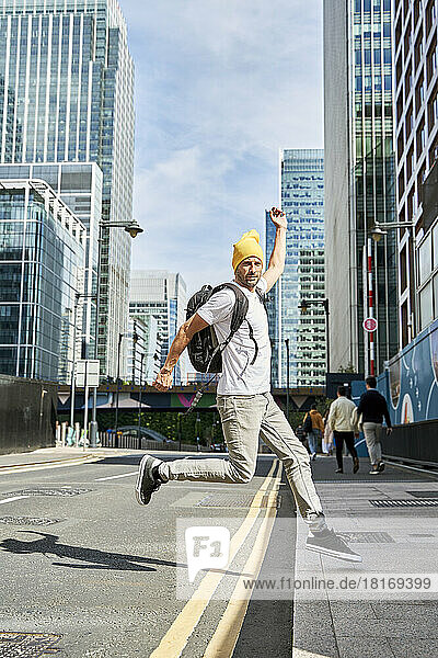 Man wearing knit hat jumping on road in front of buildings