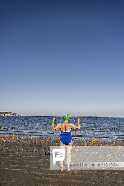 Frau schaut an einem sonnigen Tag aufs Meer und lässt Muskeln spielen