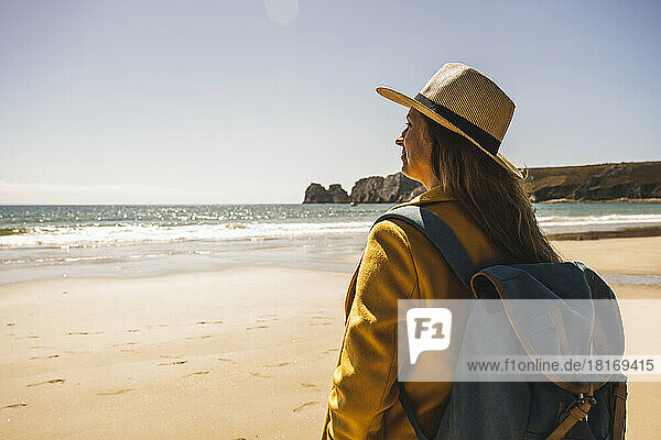 Frau mit Rucksack steht an einem sonnigen Tag am Strand