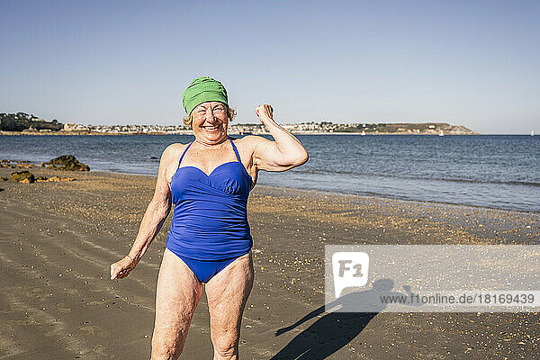Happy senior woman flexing muscle at beach