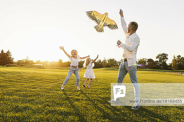 Father and daughter enjoying flying kite in park at sunset