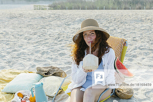 Woman wearing hat drinking coconut water at beach