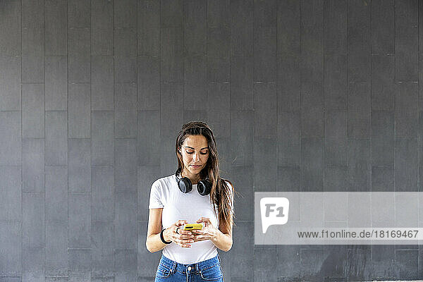 Woman using smart phone in front of gray wall