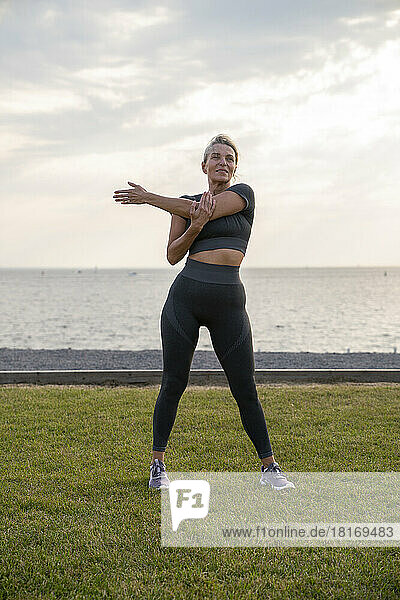 Mature woman doing stretching exercise on grass at sunset