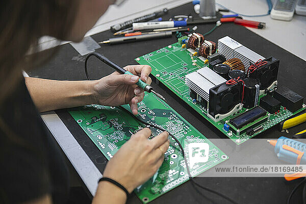 Woman soldering motherboard on table in workshop
