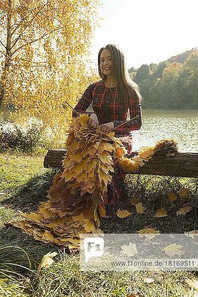 Smiling woman knitting scarf with maple leaves in park