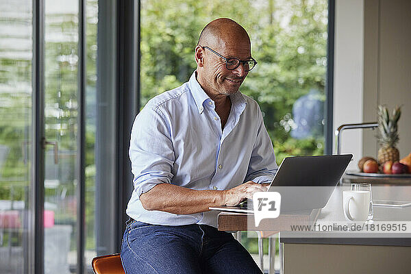 Smiling man using laptop at kitchen island
