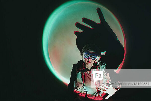 Woman wearing neon eyeglasses gesturing against black background