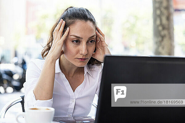 Stressed freelancer working on laptop at sidewalk cafe