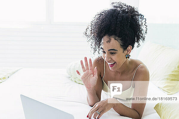 Happy woman waving on video call through laptop at home