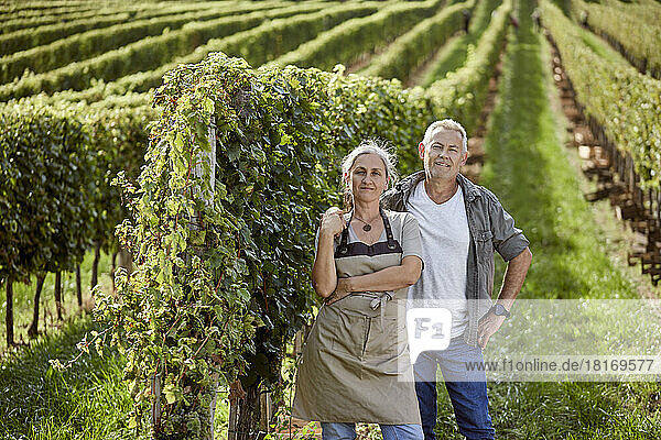Smiling mature farmers standing by grape vine in vineyard on sunny day