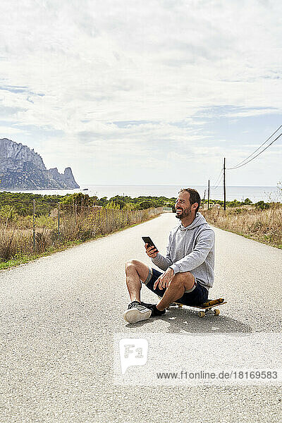 Happy man with smart phone sitting on skateboard