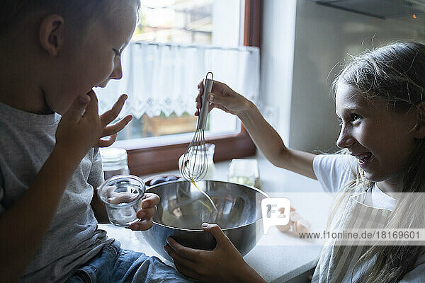 Siblings mixing ingredients for making cake in kitchen at home