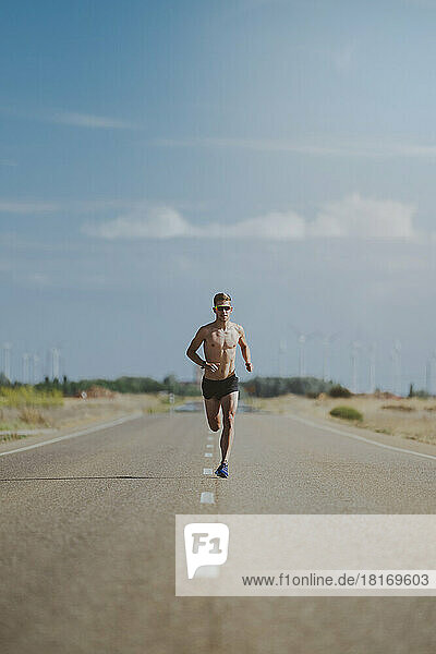 Shirtless athlete running on road under sky