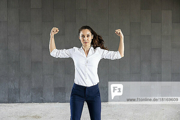 Confident woman flexing muscles in front of wall