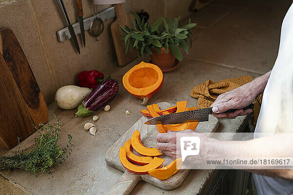 Hands of man cutting pumpkin on board in kitchen