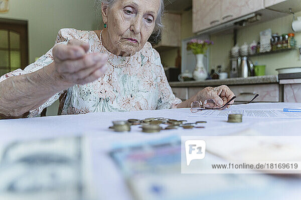 Verwirrte Seniorin blickt zu Hause auf Ersparnisse auf dem Tisch