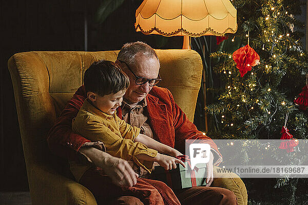 Happy grandson and grandfather sitting with gift box at home