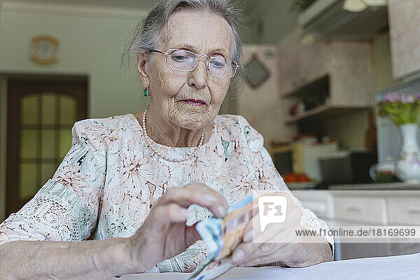 Senior woman with eyeglasses counting paper currency at home