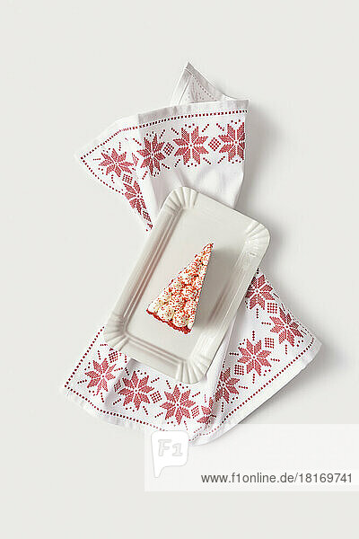 Slice of red velvet cake in white tray on embroidered table napkin against white background