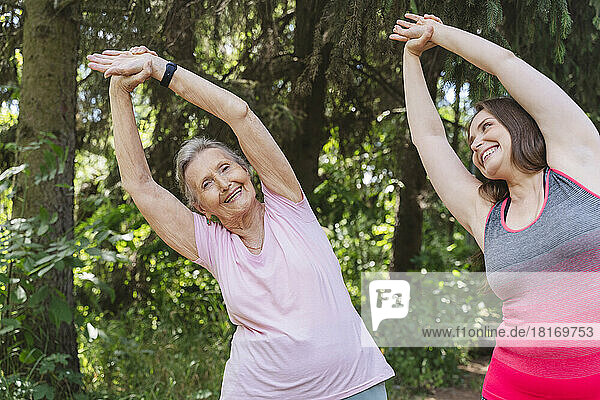 Happy fitness instructor with senior woman practicing stretching exercise at park