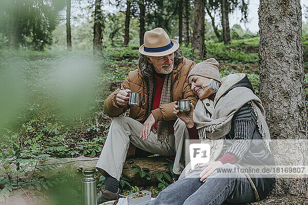 Mature woman with man having hot tea in forest