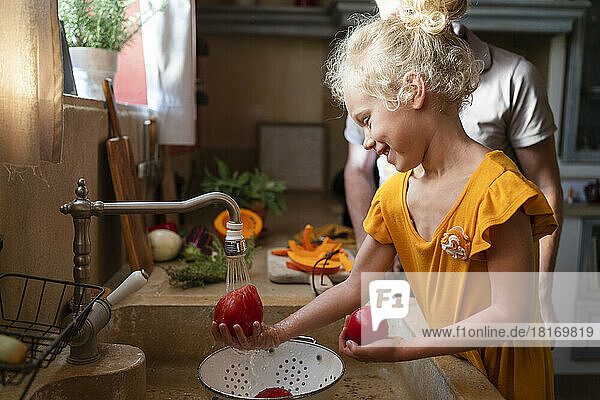Smiling girl washing tomatoes with father in background