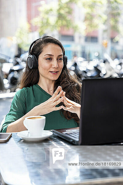 Freelancer wearing headphones using laptop at sidewalk cafe