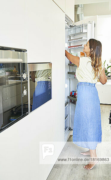Lächelnde Frau öffnet Kühlschrank in der Küche zu Hause